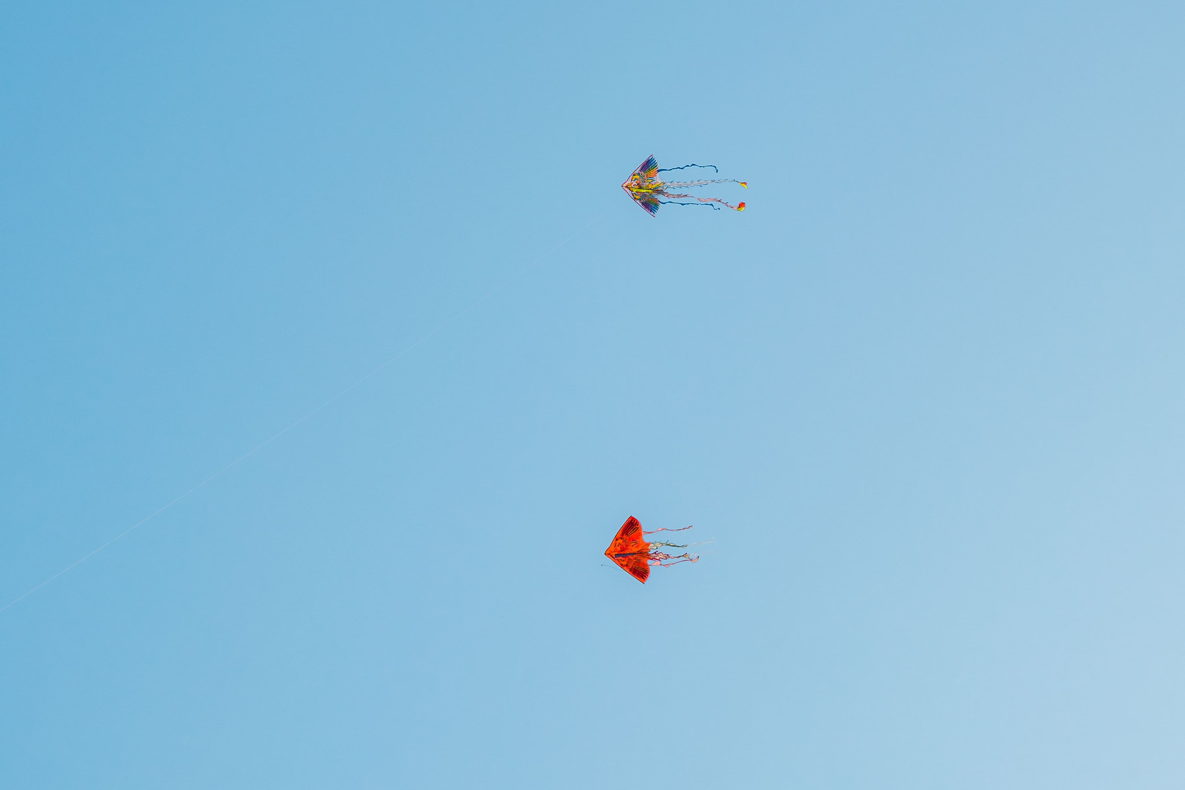 Two colourful kites flying against a clear blue sky.