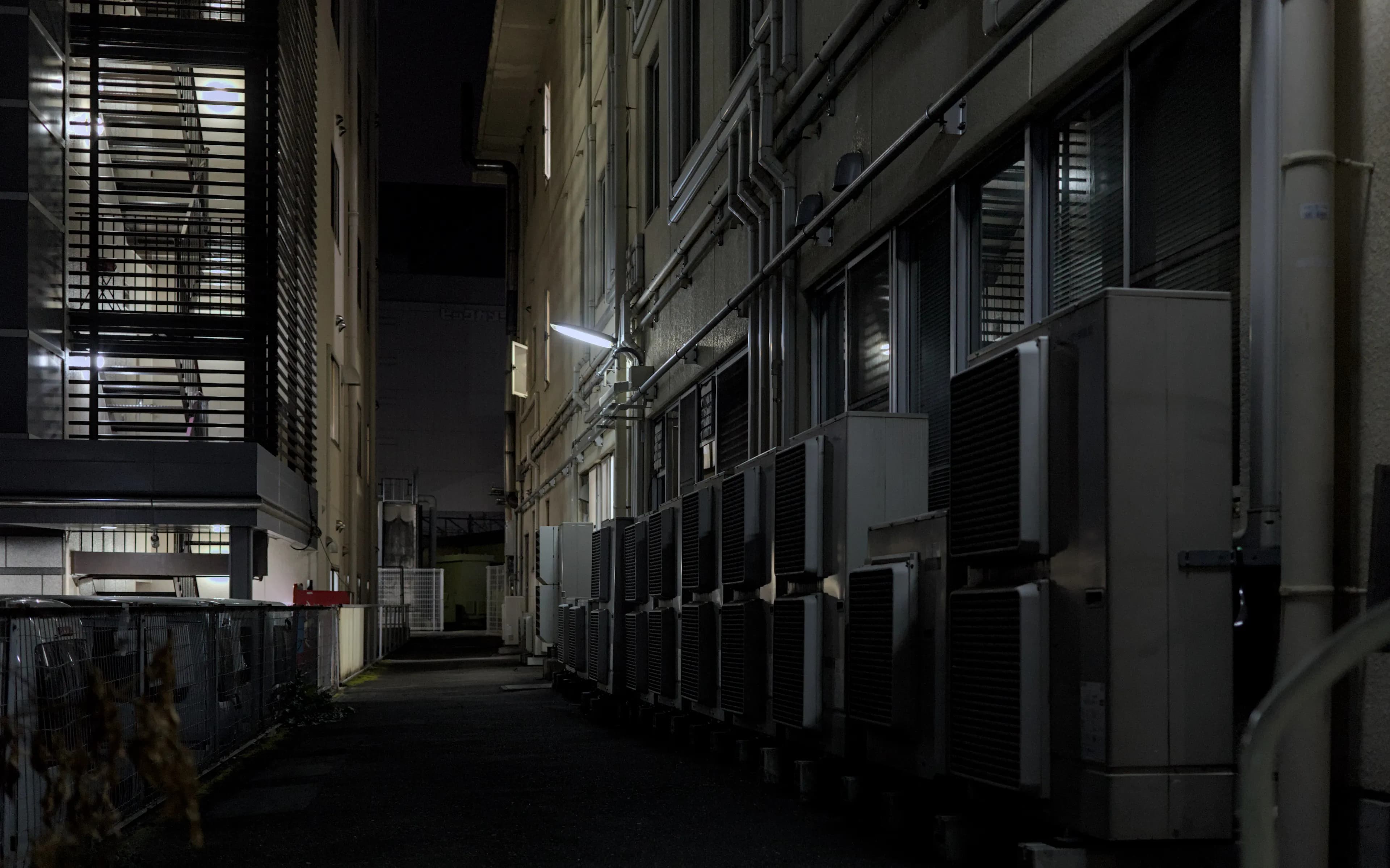 Air-conditioning units mounted on the wall of a dimly lit urban alley at night.