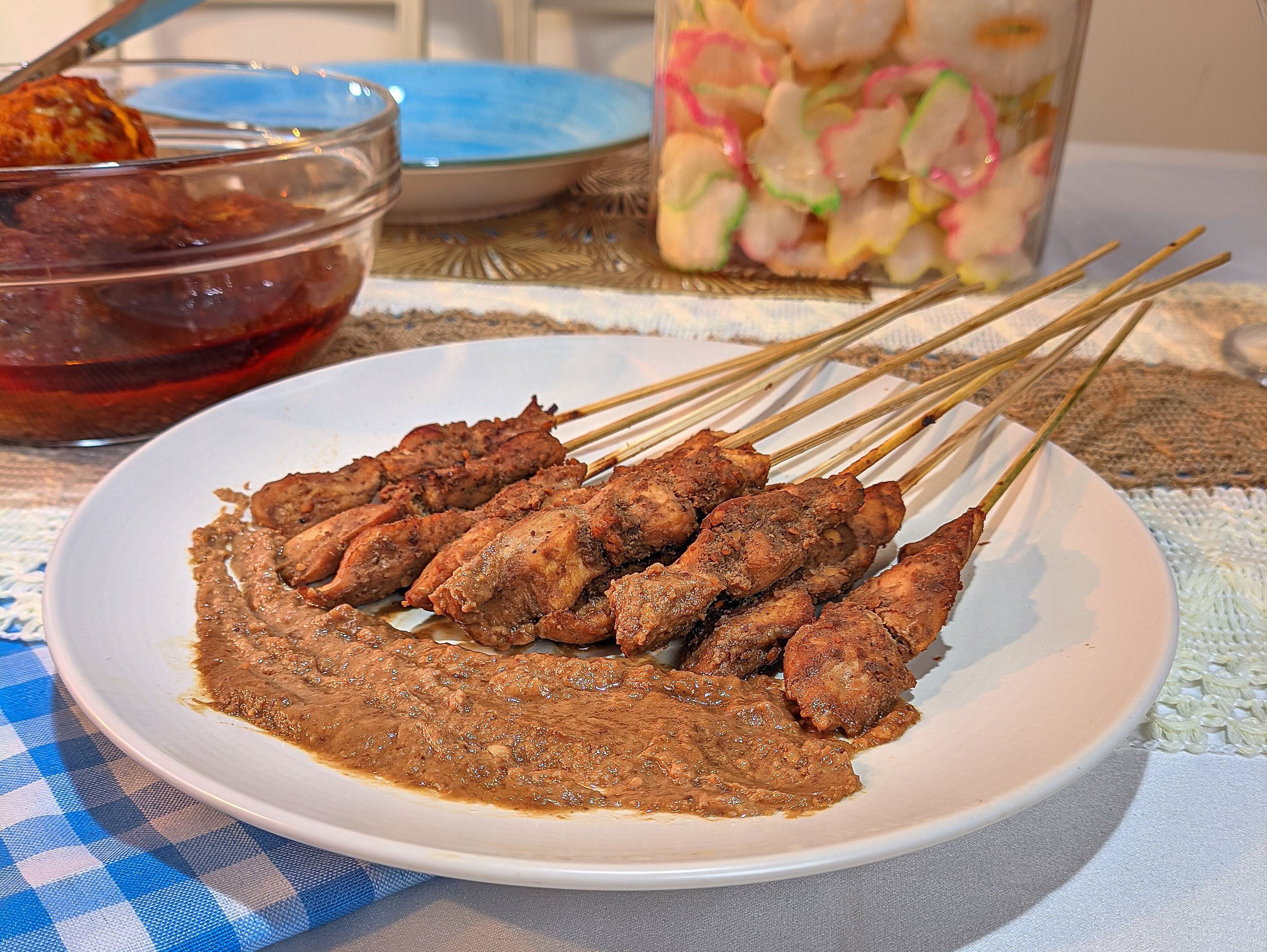 Skewers of grilled chicken satay served with peanut sauce and side dishes on a plate.