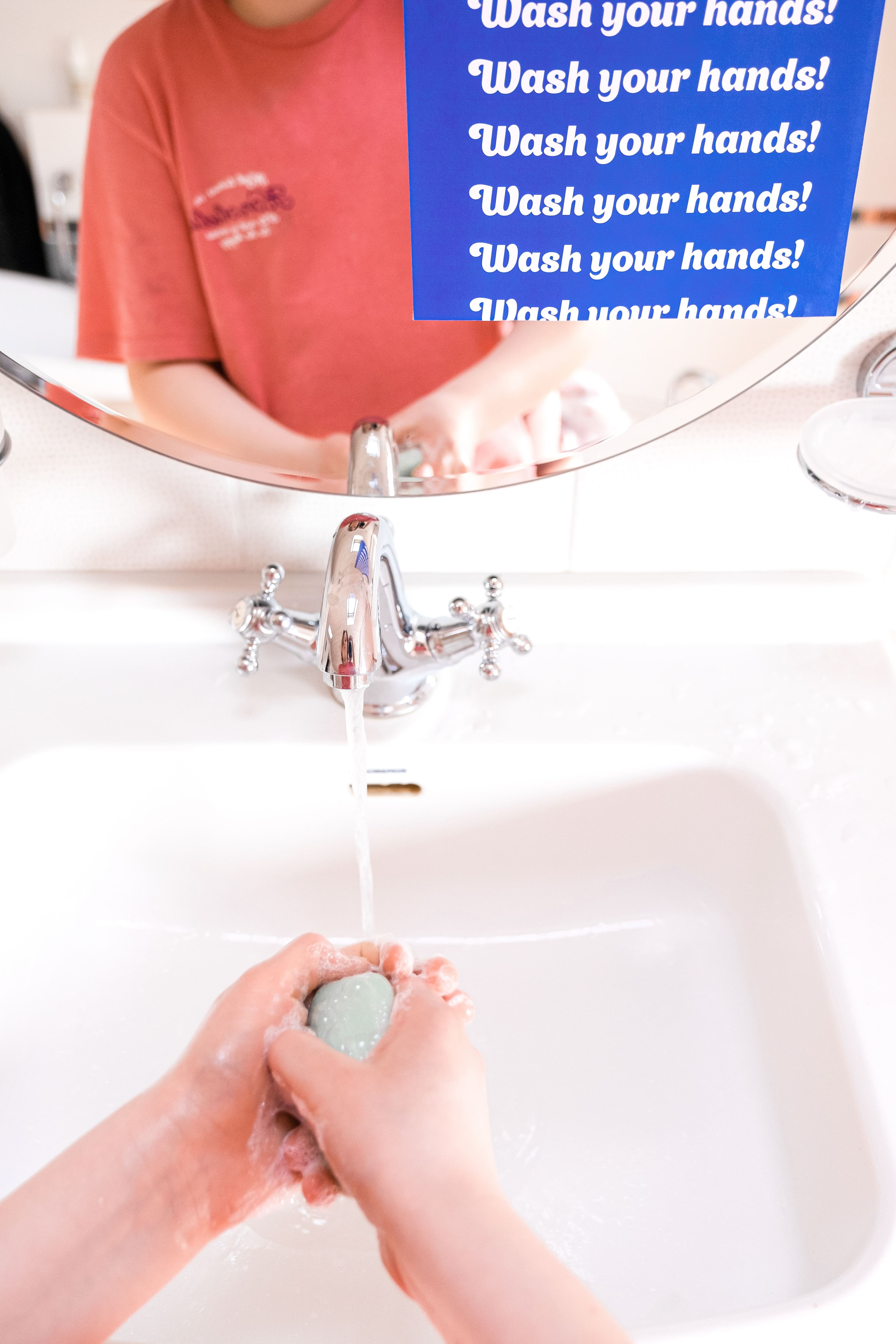 A child washes their hands with soap under a running bathroom faucet.