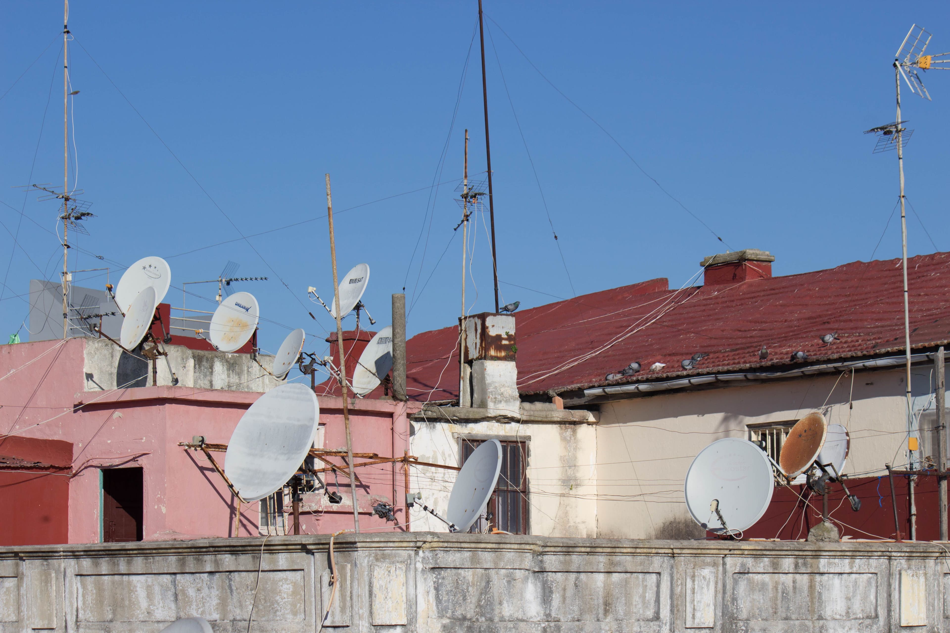 Rooftop satellite dishes and antennas mounted on a concrete building against a blue sky.