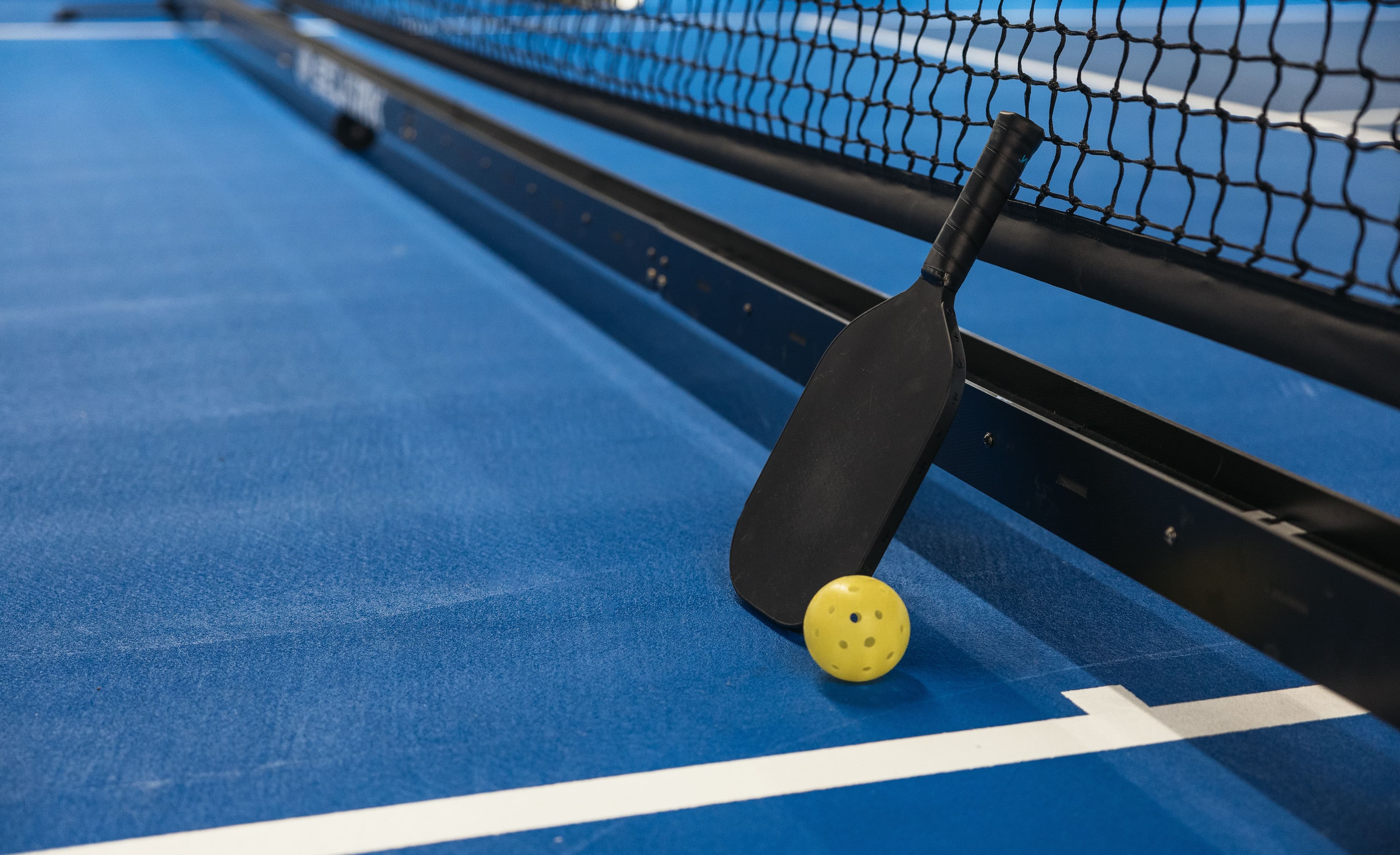 An outdoor pickleball court with paddle and ball, marked with the sport's distinctive court lines.
