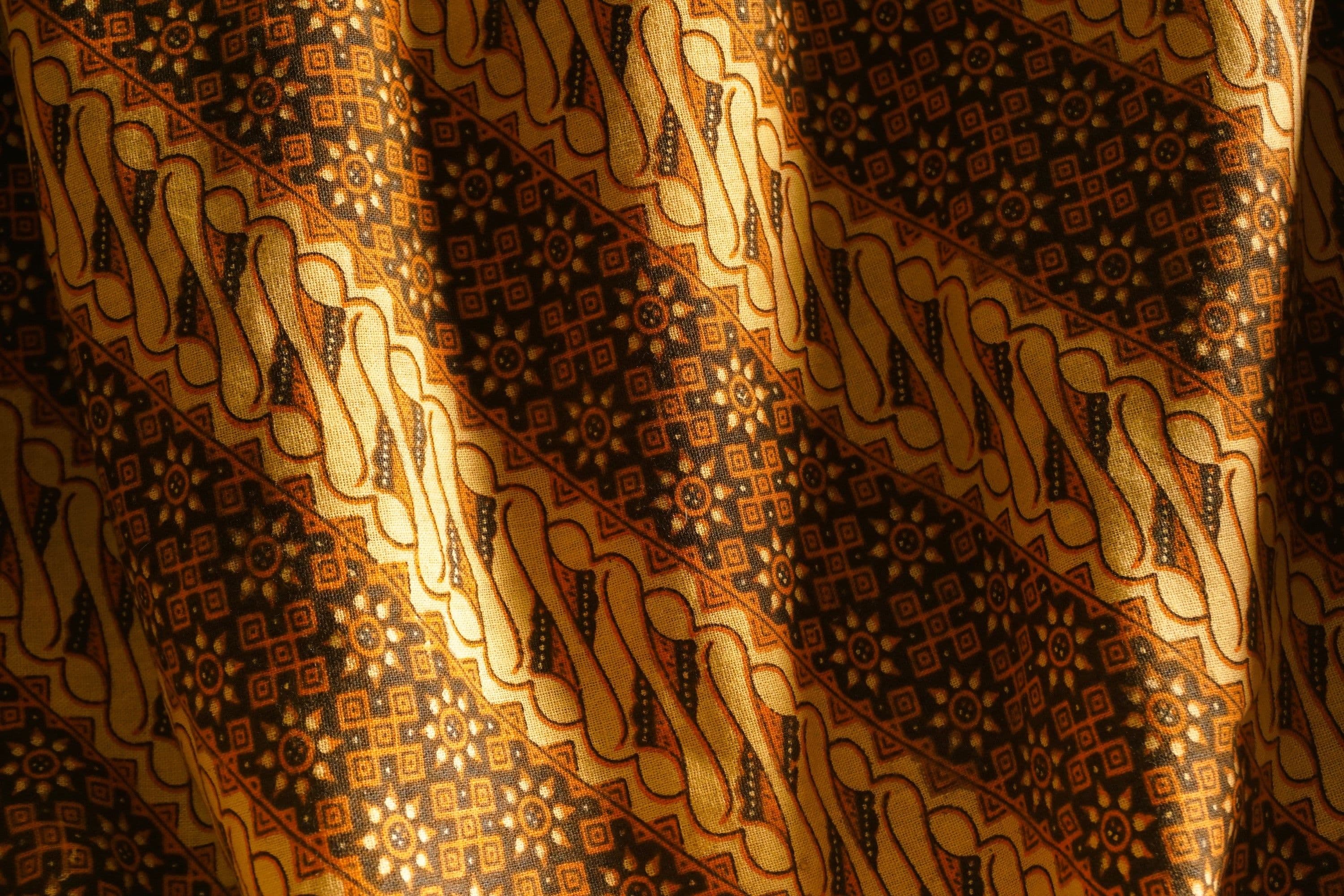 Close-up of an intricately patterned batik cloth in warm, vibrant colours, the traditional textile technique behind much of Malaysia's modern fashion revival.