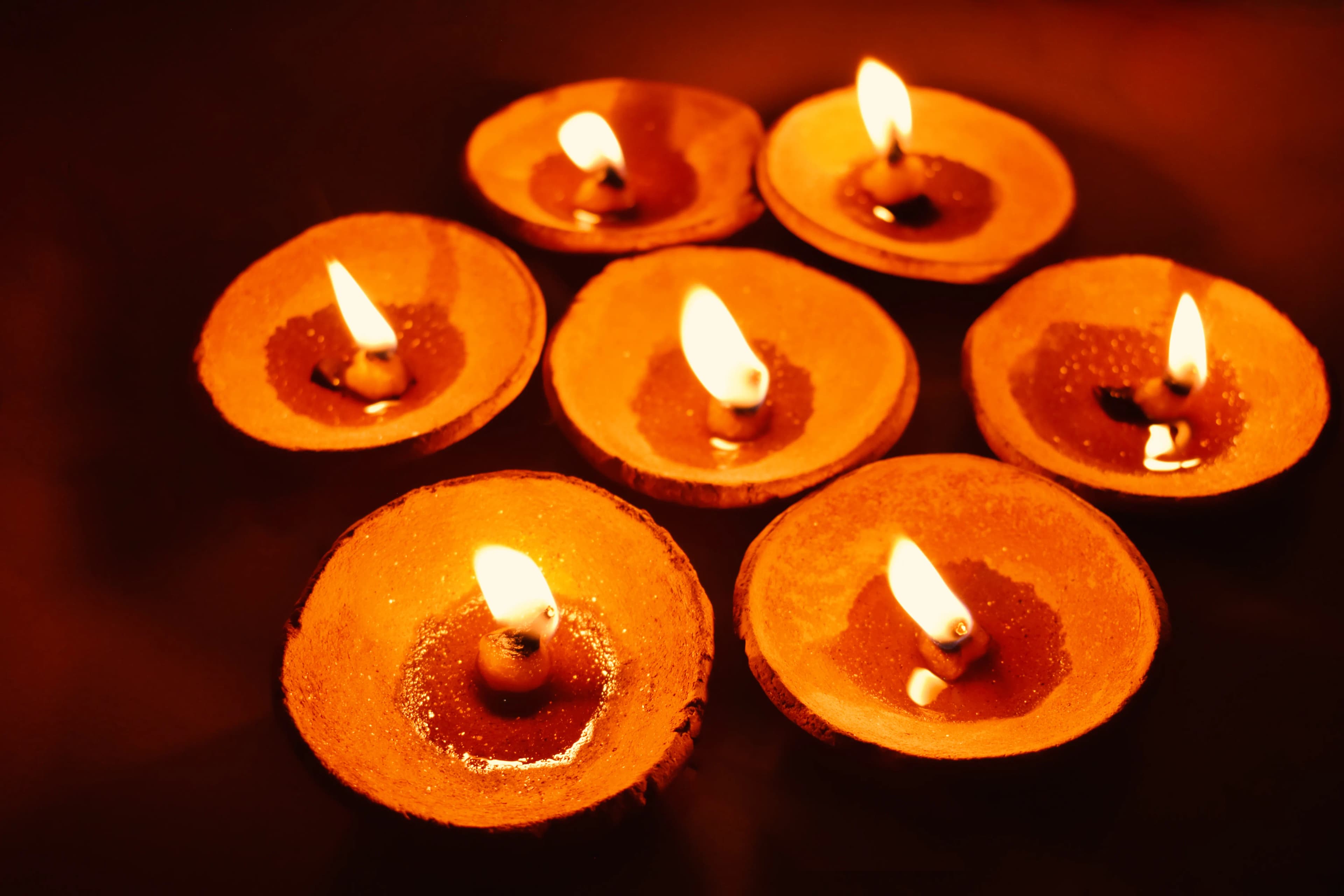 Rows of small clay oil lamps glowing warmly in the dark.