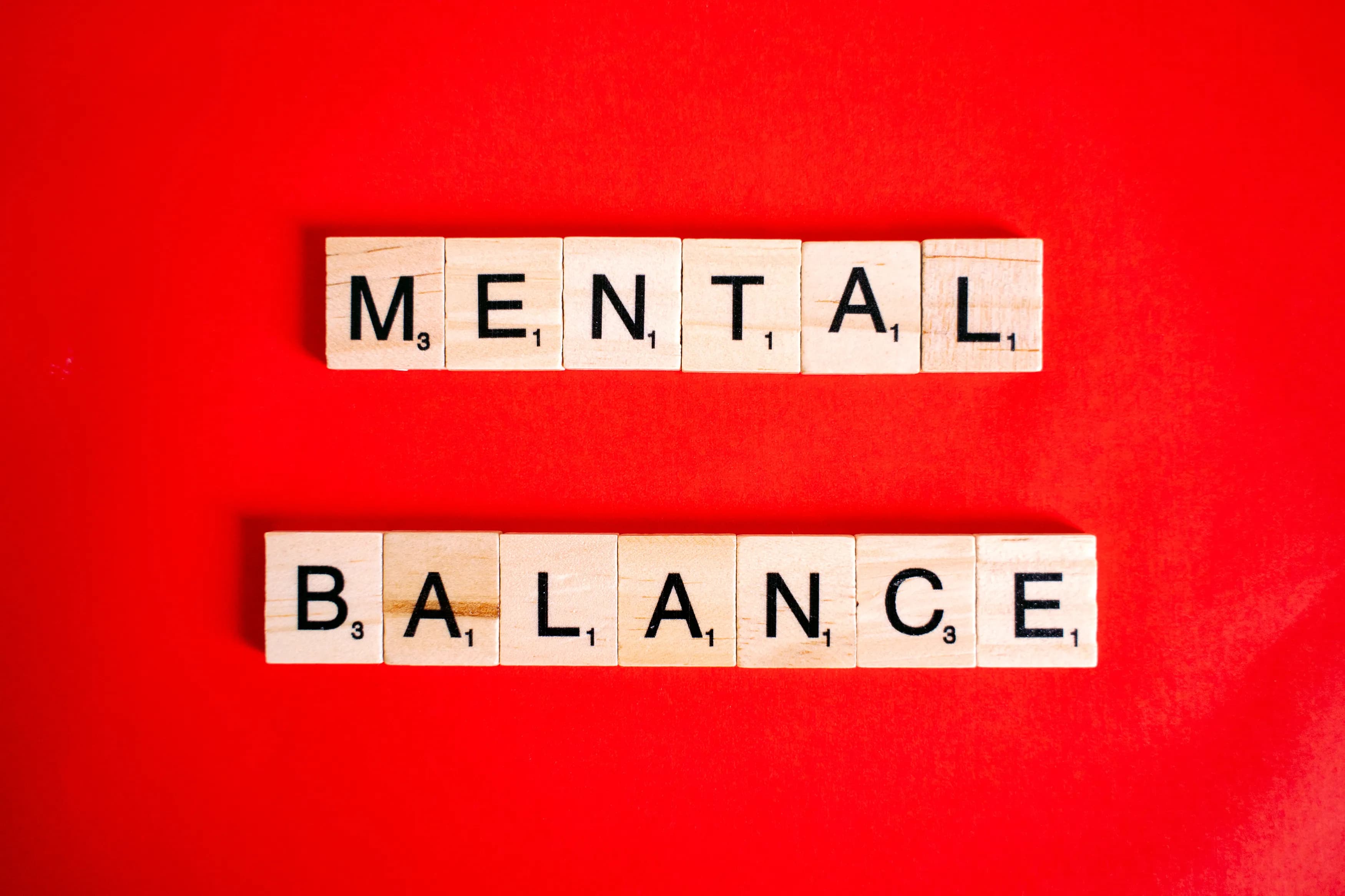 Wooden letter tiles spelling the words Mental Balance on a bright red background.